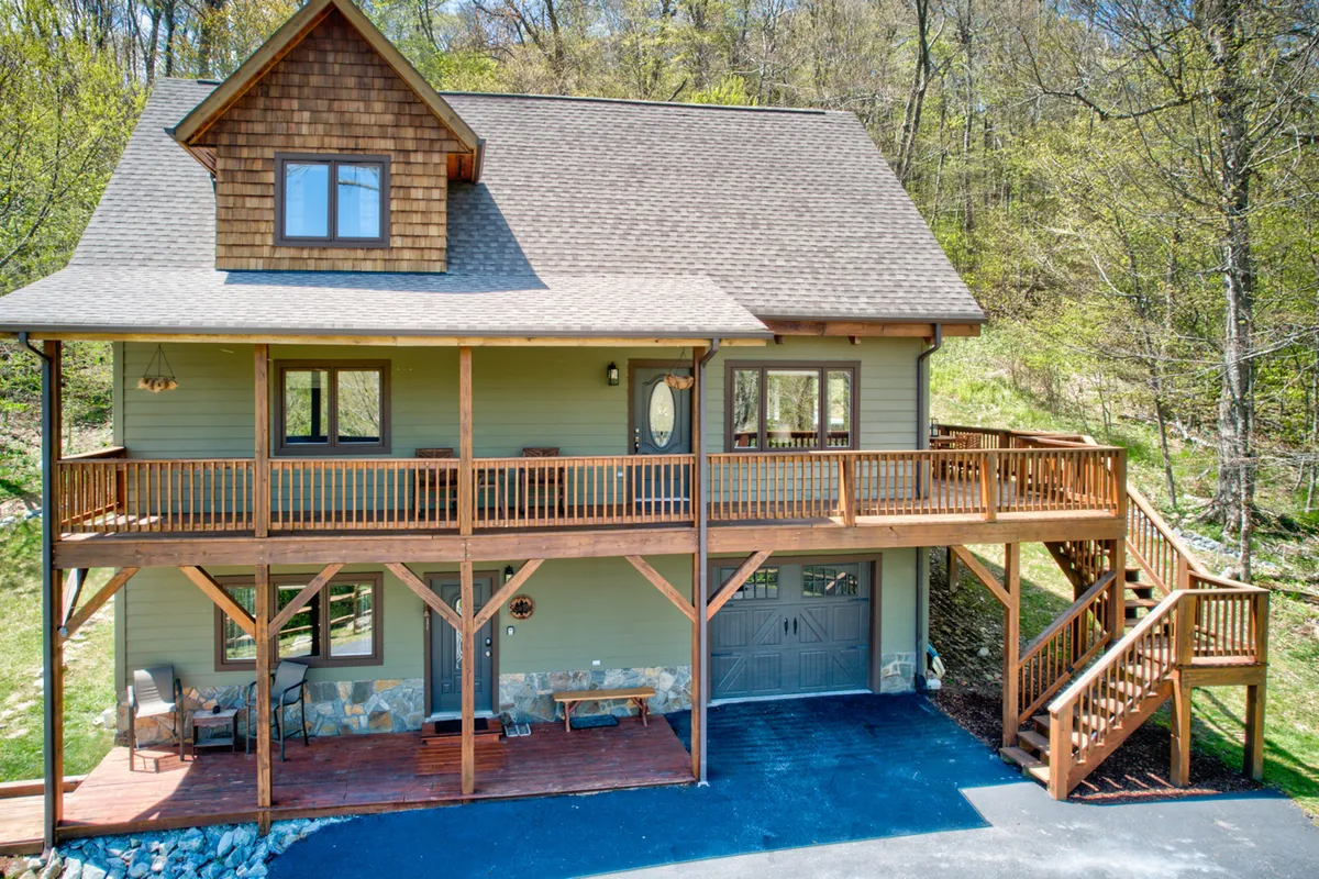 This image presents the front porch with wooden railings, stone accents, and the garage door visible. The porch is designed for gatherings and leisure, with ample space to sit or play while enjoying nature views.
