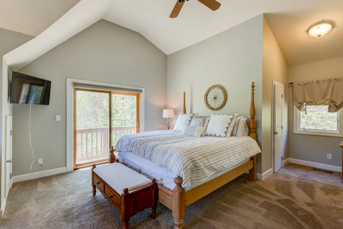 A tranquil bedroom featuring a king-sized bed dressed in plush linens, a large window streaming in natural light, a ceiling fan, and a decorative wall mirror. The neutral palette and uncluttered decor create a restful atmosphere, ideal for a master retreat.