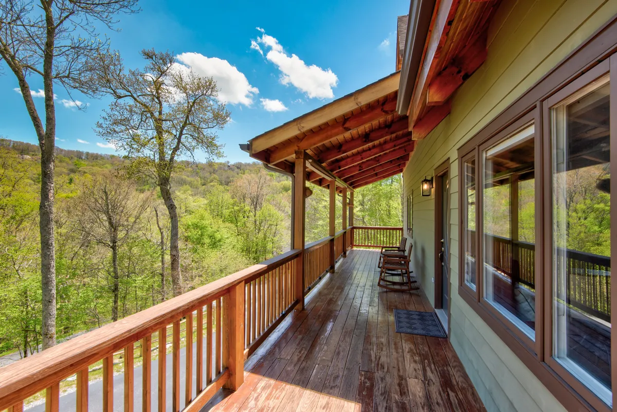A wooden deck outfitted with classic rocking chairs overlooks a picturesque backdrop of mountain views and surrounding trees. The outdoor space is positioned to make the most of sunset vistas and starry skies, with plenty of space for enjoying morning coffee or relaxing after a day on the slopes.