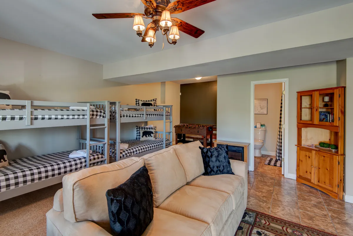 This image features another perspective on the den, with two sets of bunk beds, a cozy sofa, and a relaxed, family-friendly atmosphere. The layout invites both rest and togetherness, supporting the sleepover-style retreat described for kids and teens.