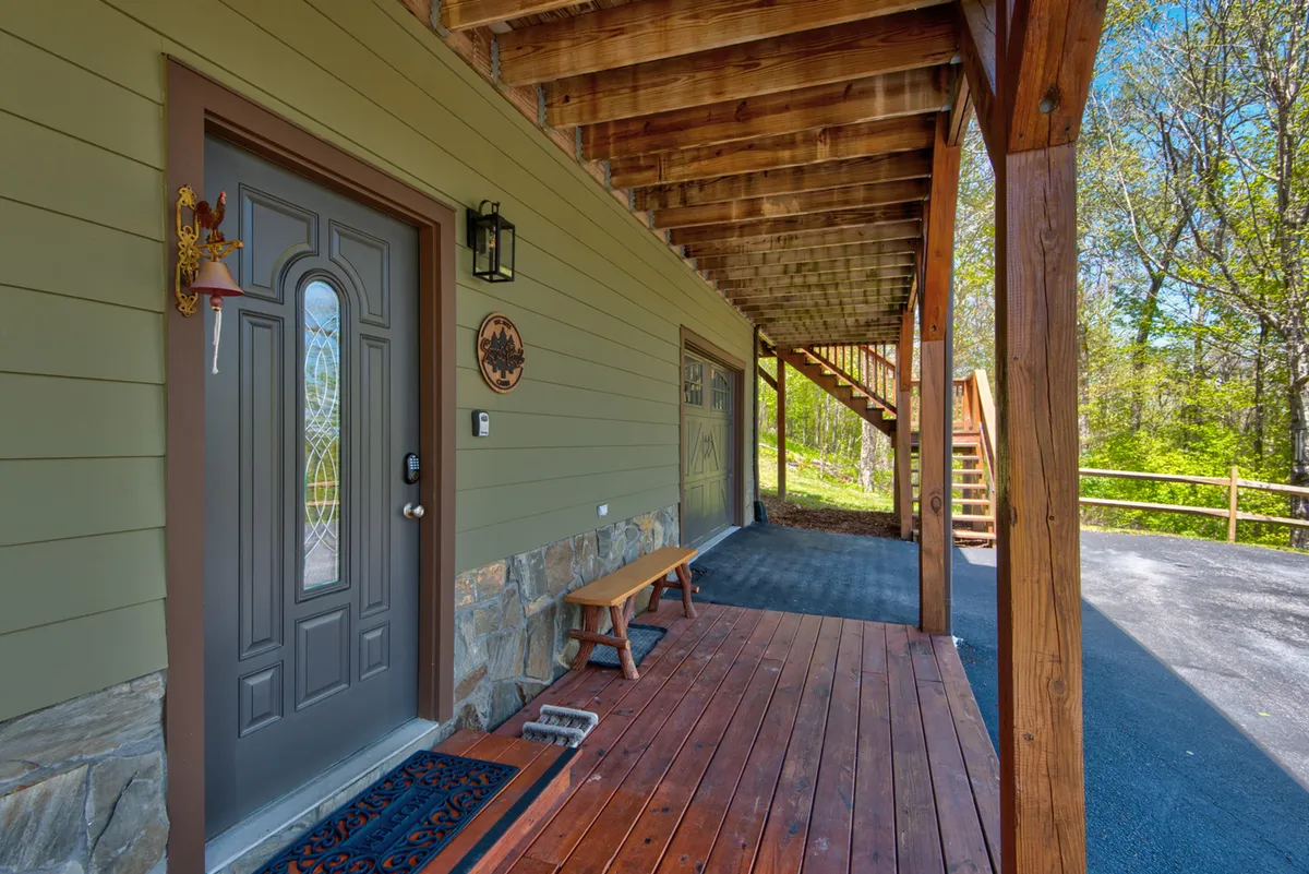 This exterior shot captures the welcoming front door of the cabin, with sturdy stonework, a wooden bench, and stairs leading up to the entrance. The surrounding greenery and inviting porch evoke a sense of arrival and serenity, hinting at the peaceful retreat inside.