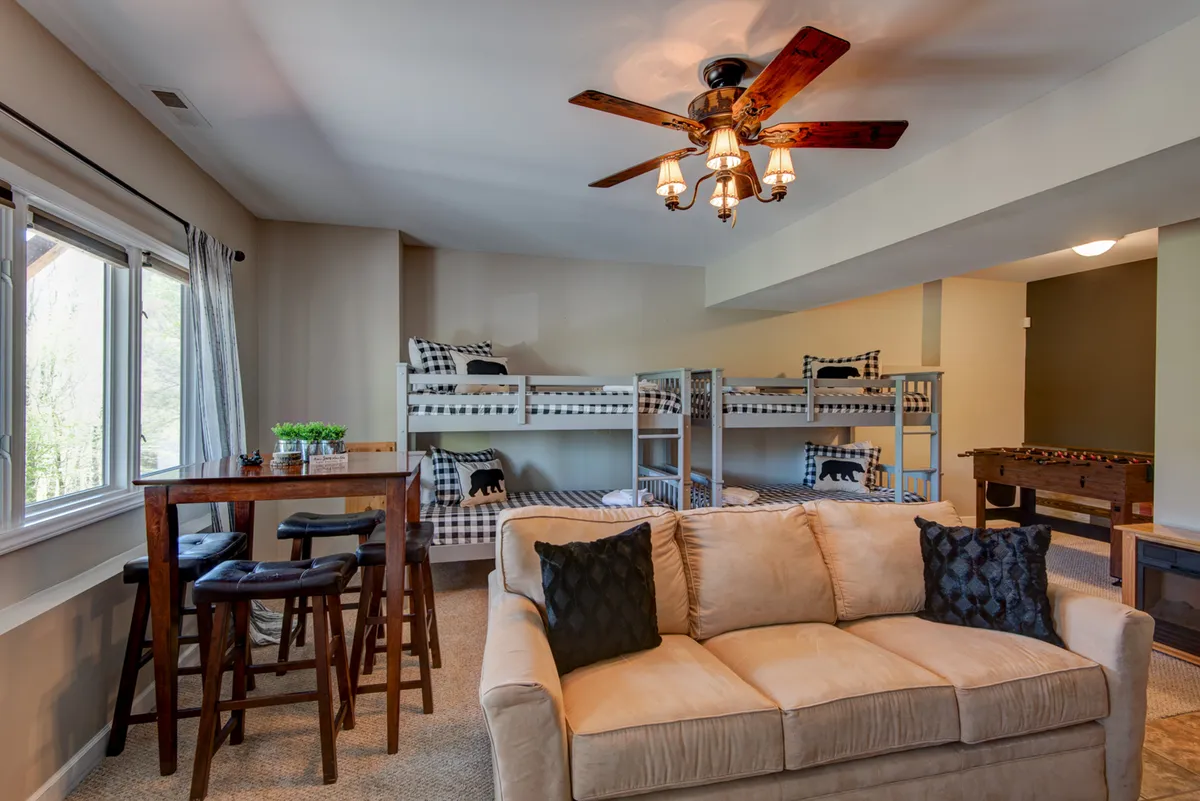 This image showcases a vibrant family den featuring two sets of bunk beds, a plush sofa, a dining table, and a pool table. The layout is open and inviting, perfectly designed for group activities, relaxation, and sleepovers. The presence of both game and lounge areas highlights the multifunctional nature of the space.