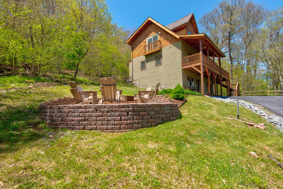 An inviting fire pit area with Adirondack chairs sits outside the home, surrounded by lush greenery and the cabin's exterior. The space is ideal for gathering in the evenings, sharing stories, and enjoying the crisp mountain air after days on the slopes.