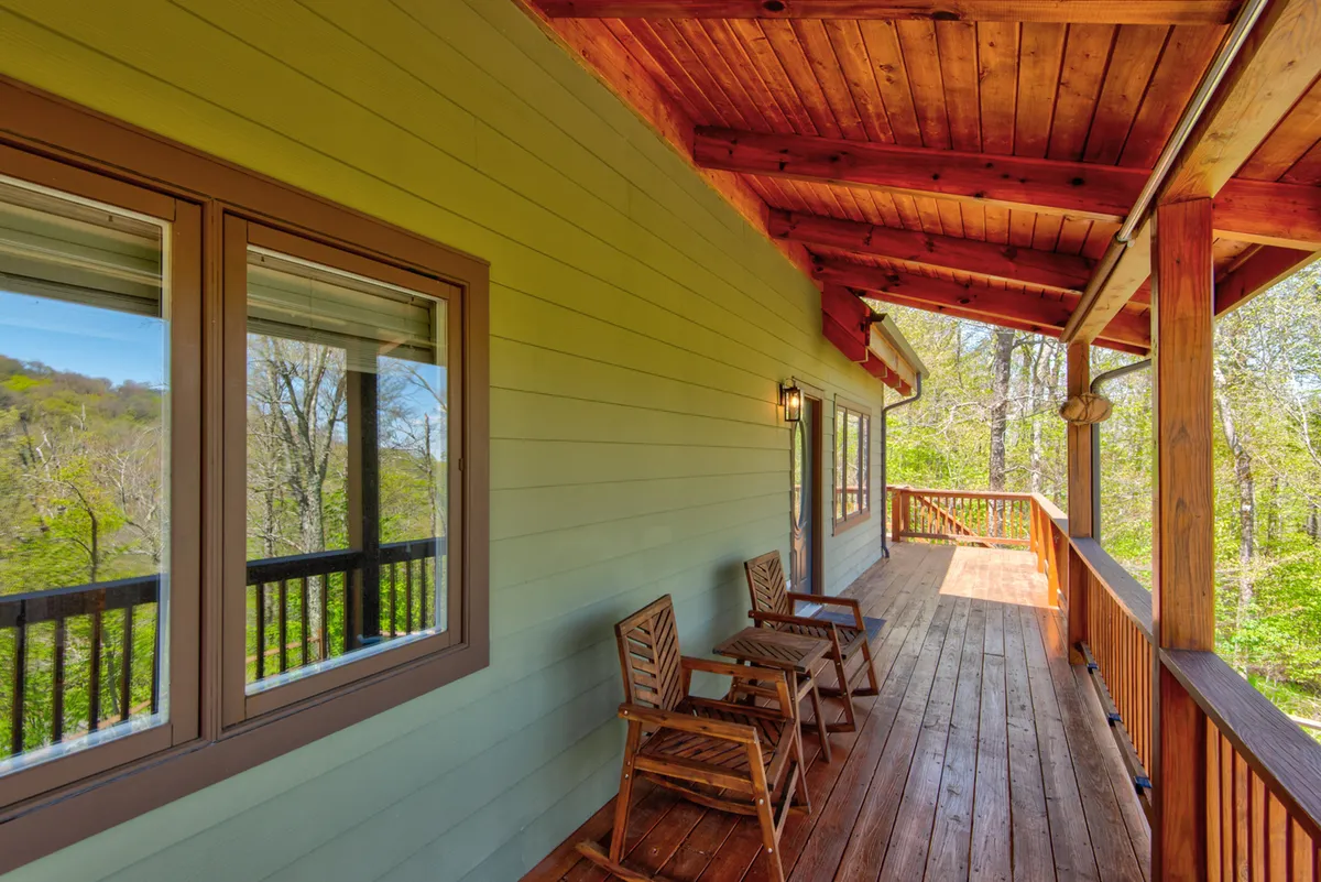 This exterior image showcases a tranquil wooden deck furnished with classic rocking chairs, surrounded by lush greenery. The railings and sturdy wooden structure create a safe, inviting space that visually connects the home to its natural mountain setting.