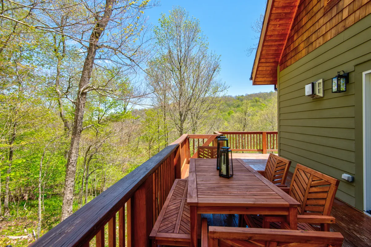 A peaceful outdoor setting on a wooden deck with a dining table, lantern, and a backdrop of tall trees. The deck provides a seamless transition from indoor comfort to nature, ideal for meals or relaxing after a day outdoors.
