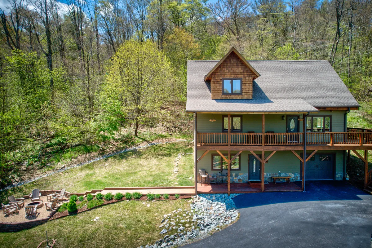 A wide exterior view showcasing the house with its welcoming porch, adjacent fire pit area surrounded by seating, and lush greenery extending into nature trails. The overall scene suggests both relaxation and outdoor adventure opportunities right at your doorstep.