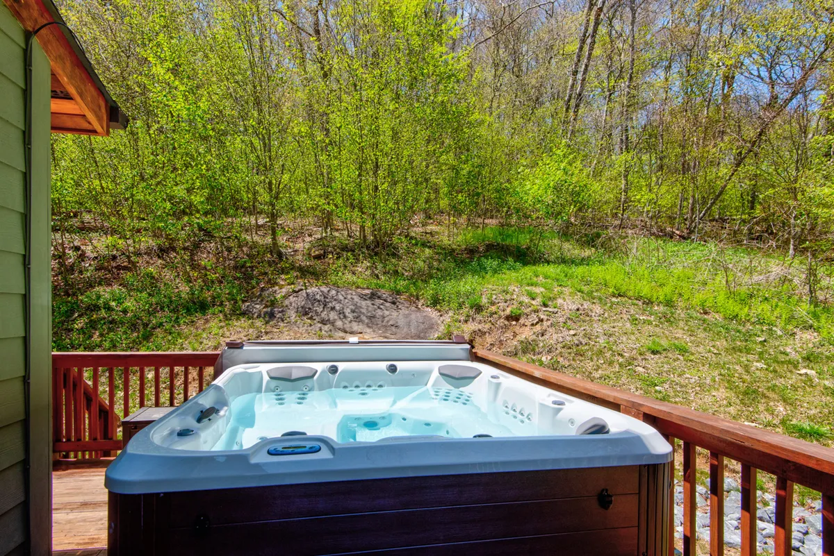 A soothing hot tub sits on the deck, surrounded by greenery and natural wood decking. The setting is tranquil, inviting guests to soak while immersed in the fresh mountain air—a perfect way to unwind and warm up after snowy adventures.