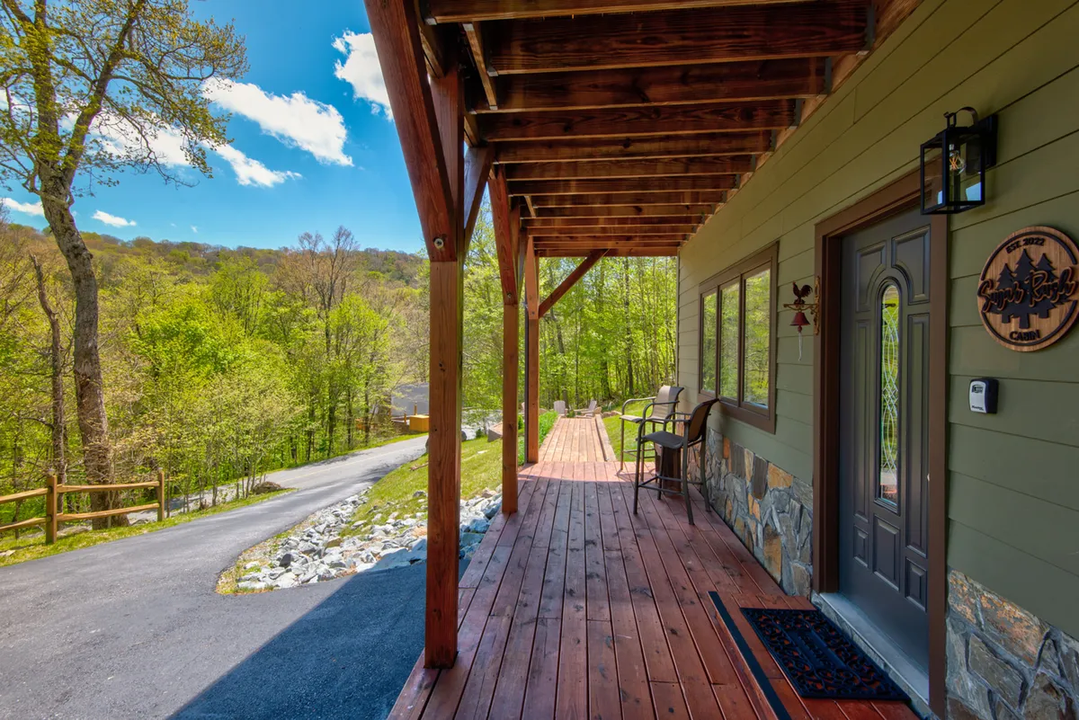 The image features the exterior of the property, highlighting a wooden porch with stone accents and a green landscape. A simple pathway leads to the porch, evoking a welcoming, family-friendly environment ideal for pets and children to play safely.